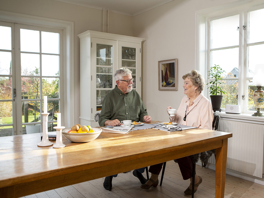 Man en vrouw aan tafel, vrouw heeft alarmketting om haar hals